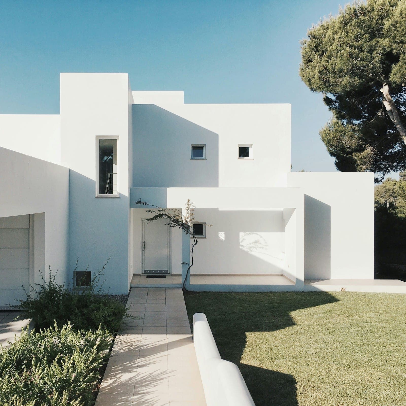 A white, minimalist Mediterranean house with a planted front garden