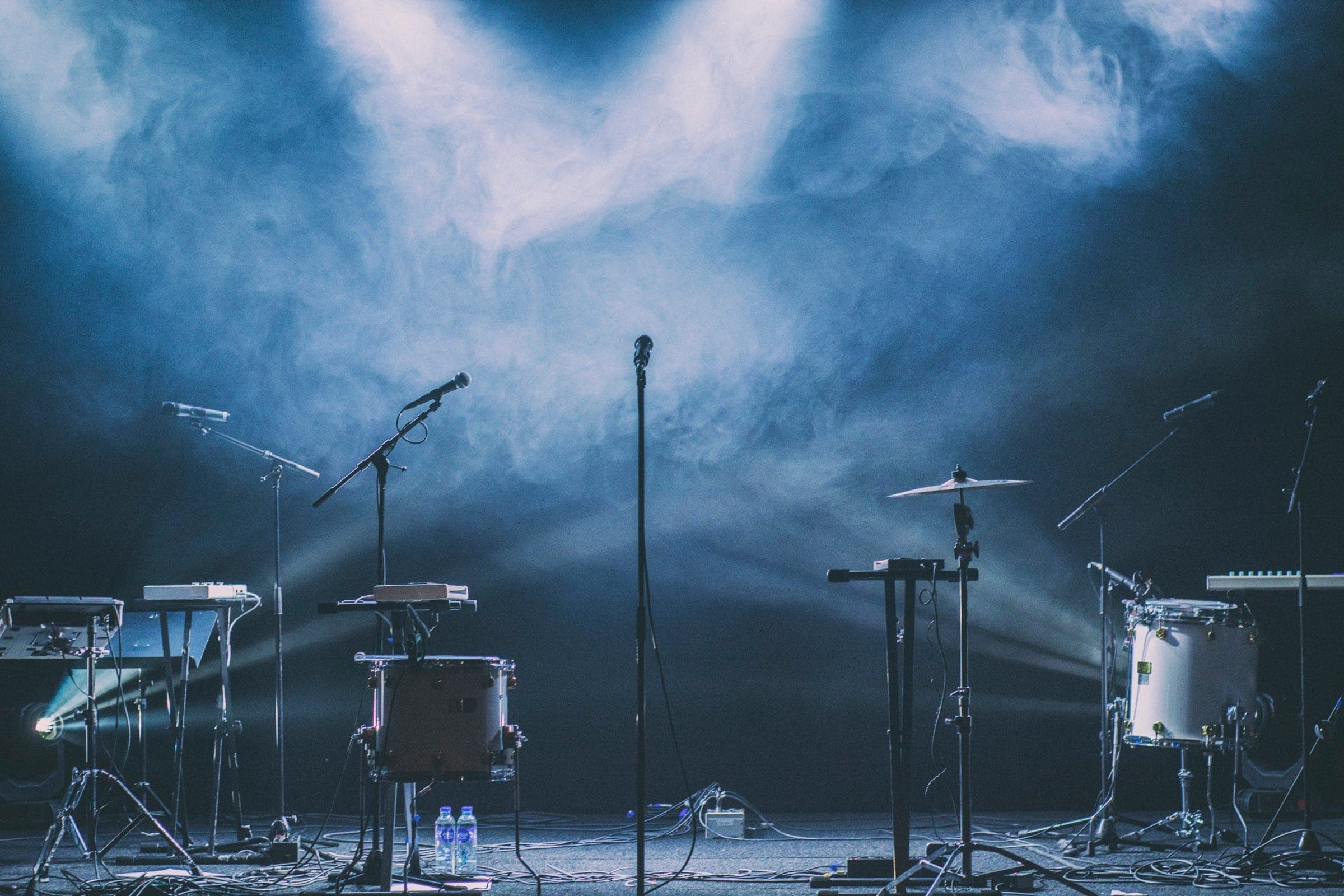 Instruments set up on an empty stage, lit by blue spotlights through haze